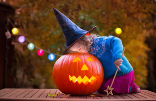A little girl in a witch hat examining a lit jack o lantern