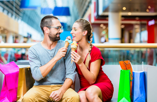A in a mall eating ice cream cones, surrounded by shopping bags