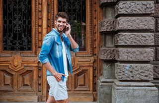 A man in a denim shirt talking on his cell phone in front of a large carved wood door
