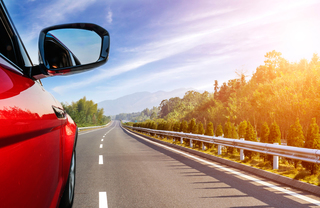 A red car on the highway headed into the hills
