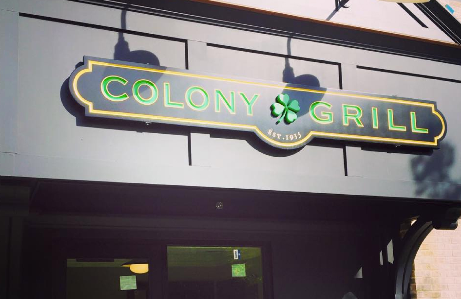 horizontal navy and green Colony Grill restaurant sign with a shamrock in the center - The Waypointe Apts