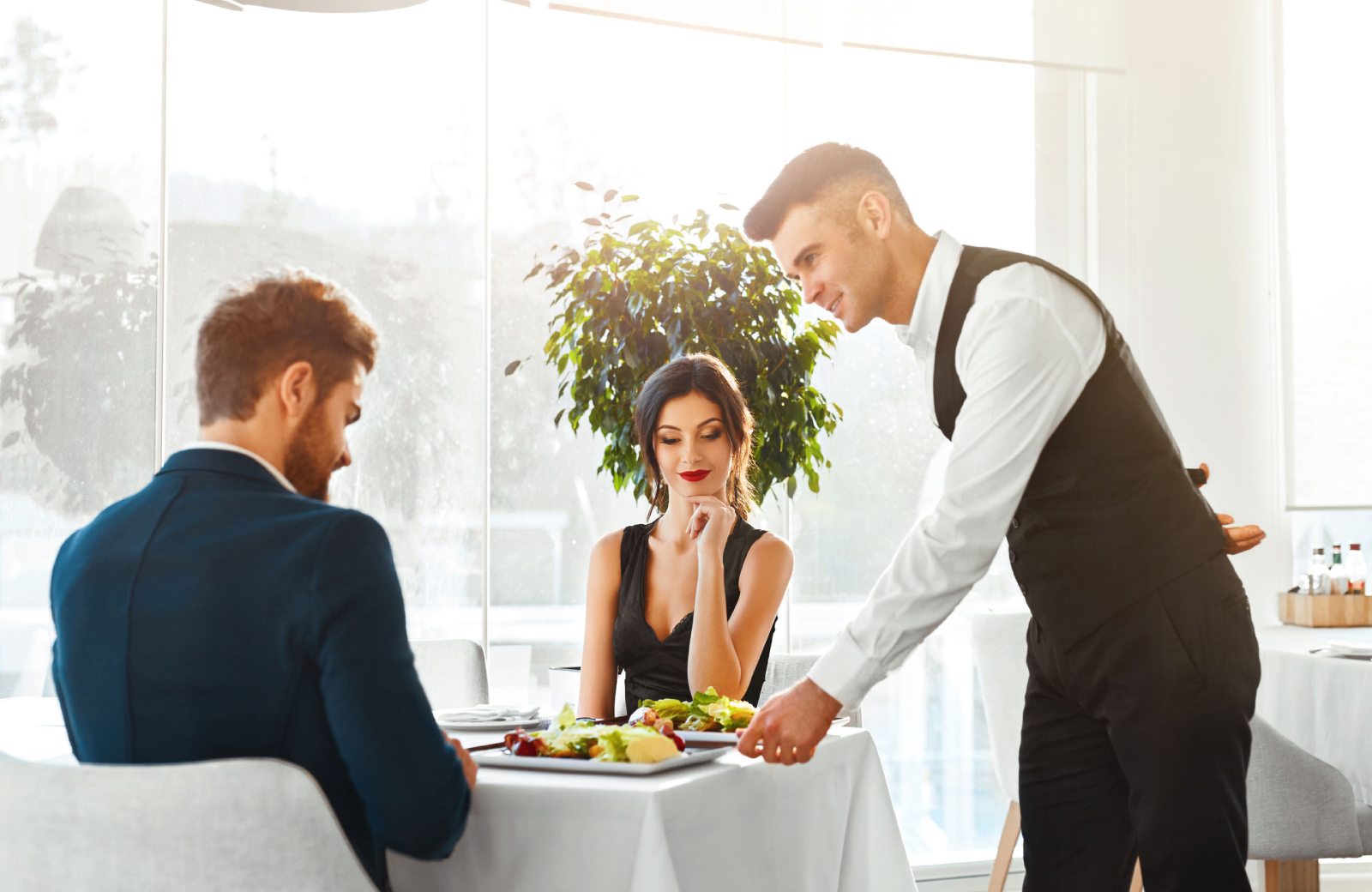 waiter delivering food and a bottle of wine to a couple having a fancy dinner in SoNo - The Waypointe Apartments