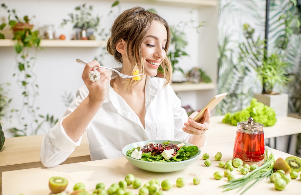 a woman in a white button down shirt eating a salad while looking at her phone - The Madrid westchester ca apartments