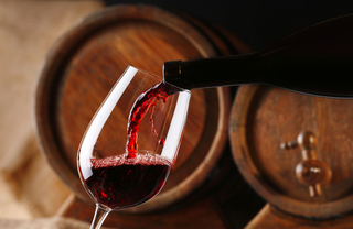 Red wine being poured into a glass in front of barrels of wine