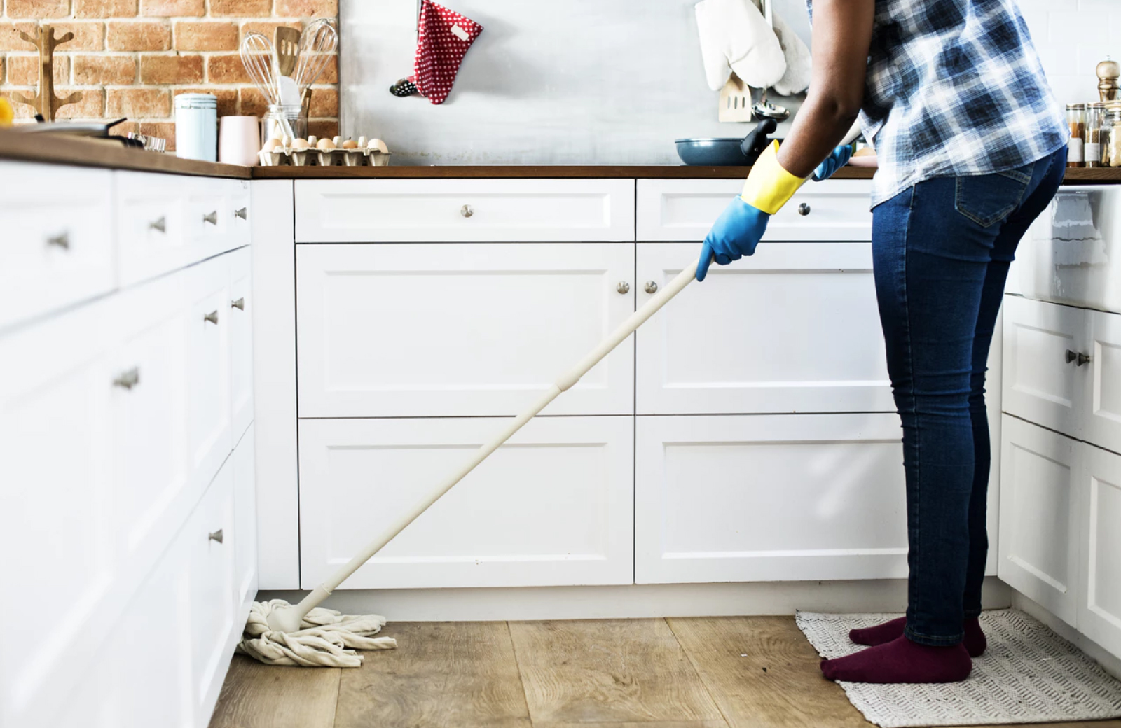 legs of a woman mopping the kitchen floor with green cleaning tools near white cabinets - The Waypointe