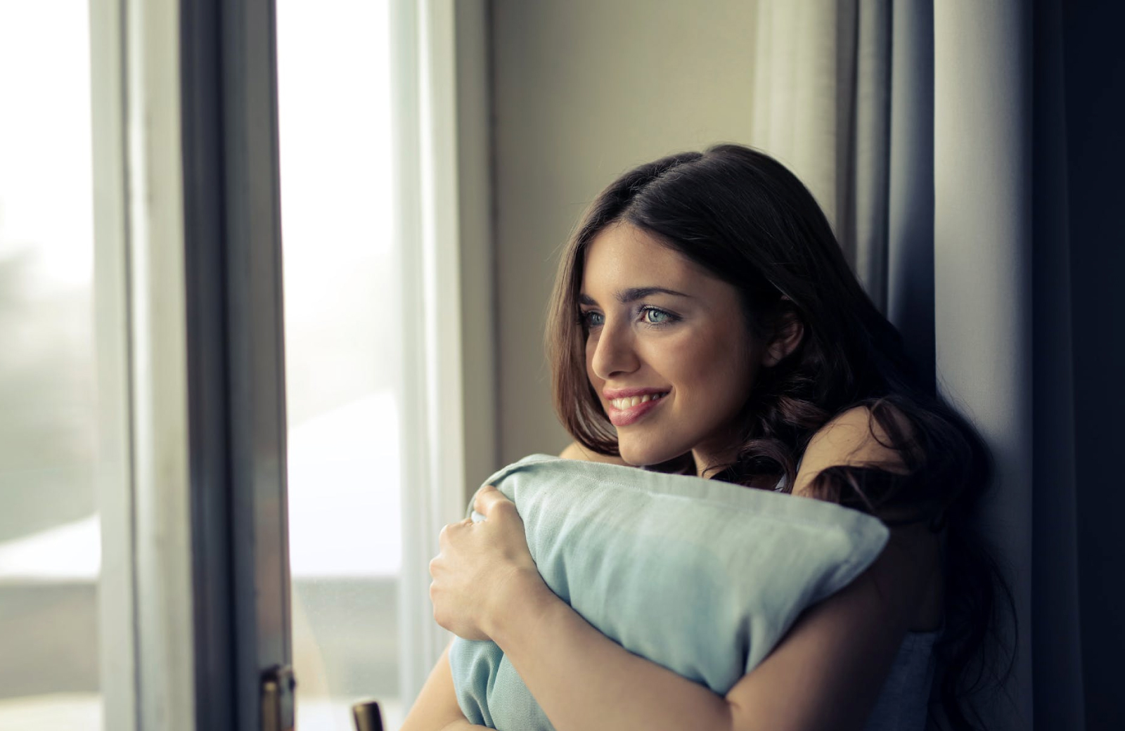 woman with brown hair holding a pillow looking out the window - madrid townhomes