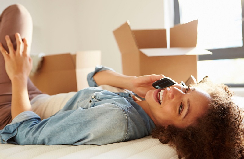 woman with dark hair in a denim shirt laying back on the couch talking on cell phone - The Madrid Westchester LA apartments