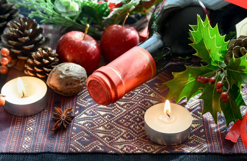 close up of the top of a wine bottle with candles and sprigs of holly for drink gift ideas - The Madrid LA