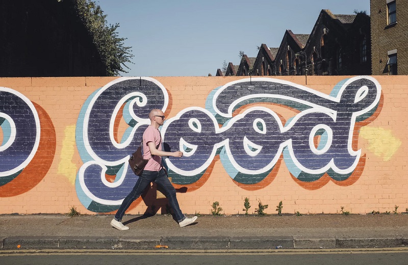a guy walking down the sidewalk in front of a mural that says "GOOD" in downtown LA - The Madrid Apts Westchester