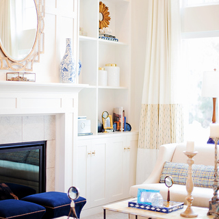 A bright apartment interior, with white shelving, a fireplace with a white mantle, and an off white sofa