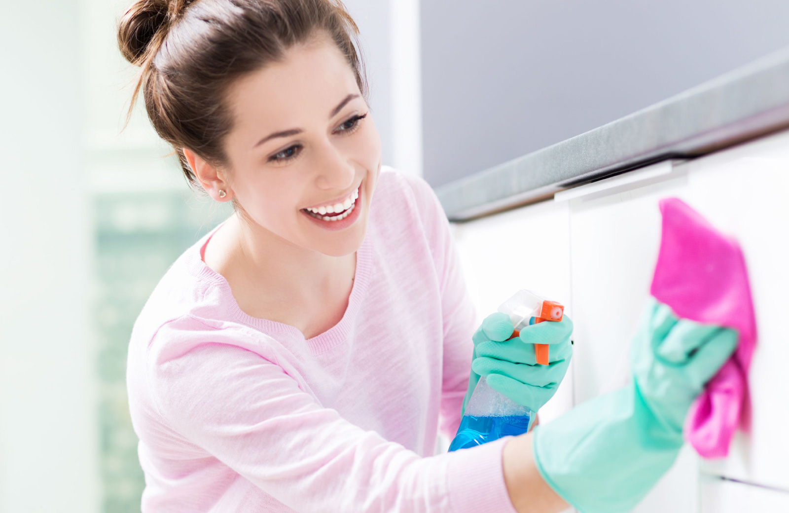 woman in green latex gloves happily wiping off her white cabinet doors - waypointe apartments