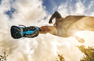 Upward shot of a runner mid-air against a blue sky