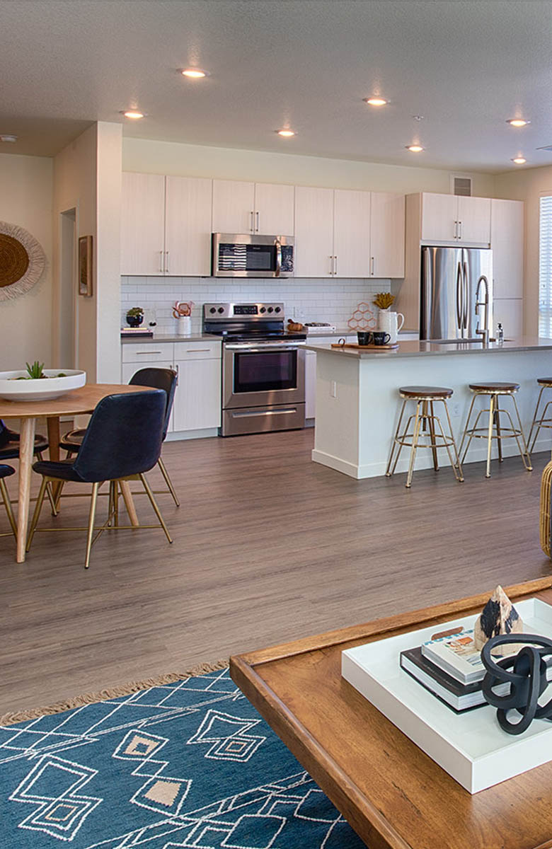 Large open living space with couch and coffee table, and adjacent kitchen with island, barstools and entryway,