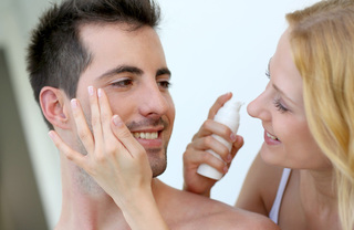 closeup of woman with blonde hair happily applying moisturizer to man with dark hair - Waypointe Apts