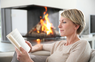 Woman reading book by the fireplace.