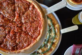 A close-up view of a deep-dish pizza topped with rich tomato sauce and herbs, served on a raised stand, with another thin-crust pizza in the background at The Star on Park in Alameda.