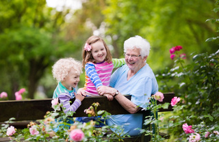 smiling grandma and two young kids sitting on bench in the garden
