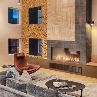 A lounge area with a linear fire place, a blue velvet sectional, and two burgundy leather armchair