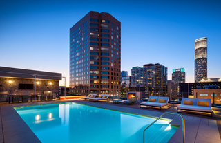 A rendering of the rooftop pool lit up at night, with a bar and cushioned lounge chairs on deck