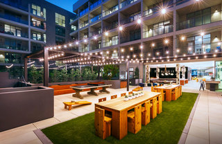 A rendering of a building courtyard with multiple gas grills and dining arrangements illuminated by string lights
