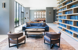 A couch and two chairs sit adjacent to floor-to-ceiling bookshelves with blue books in the Atelier Business Lounge