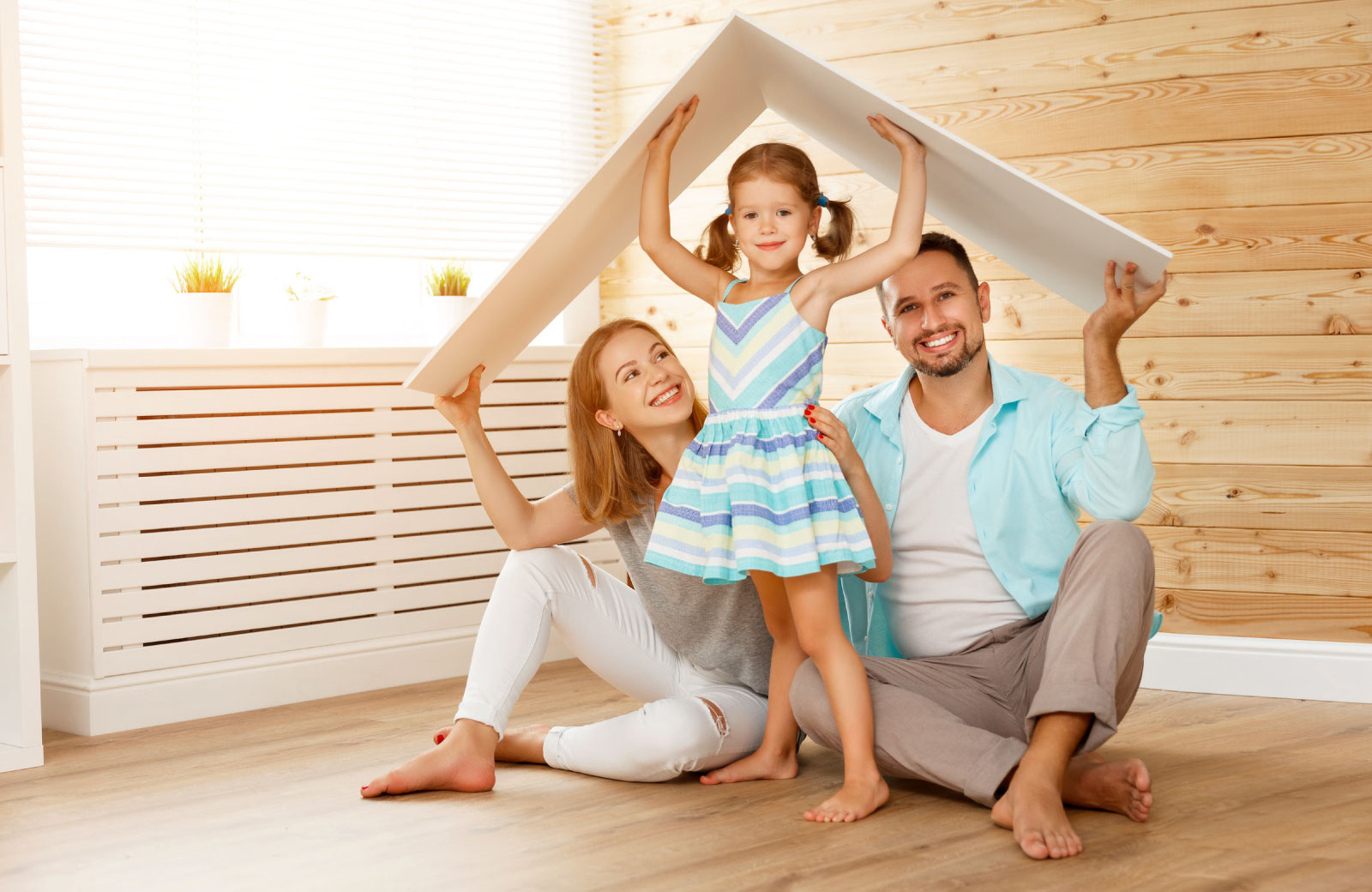 family of three with mom dad little girl holding up a thin piece of wood over their heads