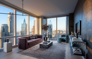 A large living room with a velvet couch, marble coffee and side tables, a floral patterned armchair, and floor to ceiling windows.